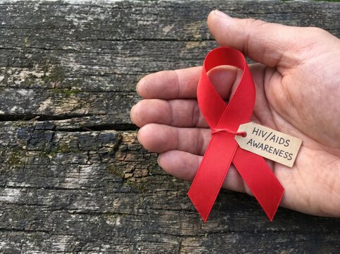 Hand holding red awareness ribbon with tag for HIV and AIDS awareness day on old wood table