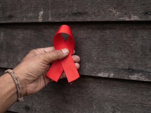 Man holding red ribbon symbol for world aids day awareness against rustic wooden background