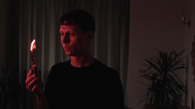 Man contemplating revenge while examining a knife at home, reflecting on a dangerous decision and consequences in a dark cinematic interior with warm red light and psychological tension