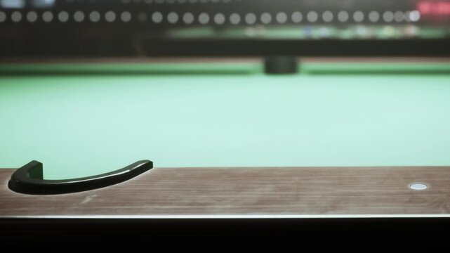 Under the warm lights of a busy game room, a close up captures the elegant curve of a pool tables edge. The vibrant green felt invites players to enjoy their spirited matches.
