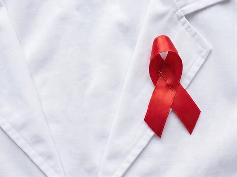 Red awareness ribbon pinned on a white doctor coat symbolizing HIV and AIDS campaign symbol care
