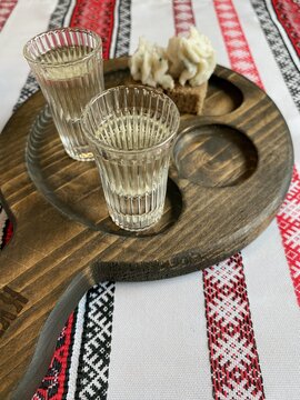 Two shot glasses of vodka and a slice of bread with salo on a wooden board.