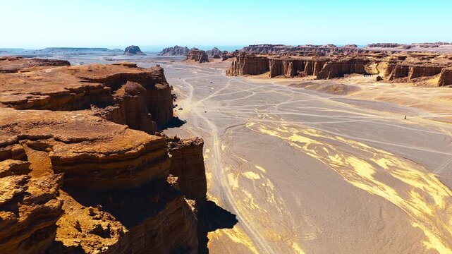 High angle shot shows majestic yardang landform cliffs and vast arid valley in Dahaidao desert under bright sunlight.