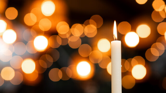 A lit white candle with a warm backlight and a blurry bokeh effect