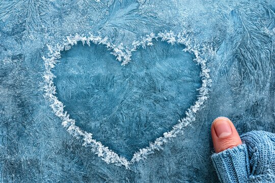 Heart shape drawn on frosty window pane with finger in winter mood