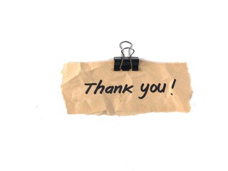Handwritten thank you note on torn brown craft paper held by a black binder clip isolated on white. Perfect design element for appreciation concepts, business gratitude, and greeting card templates © Eka