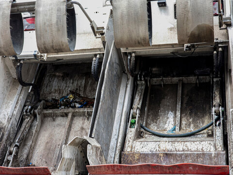 Close up view of hydraulic pressing mechanism inside a municipal garbage collection truck showing compacting system in operation