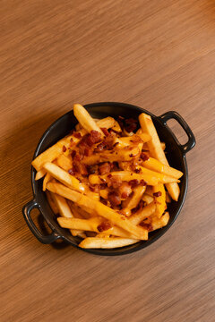 Top-down view of a portion of french fries served on a black plate with handles and topped with bacon bits.