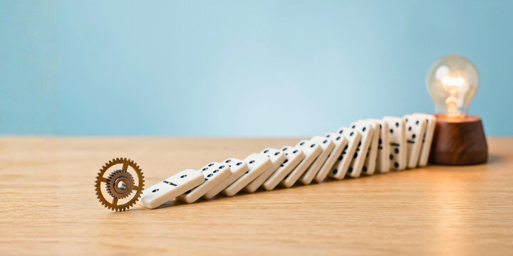 Domino chain reaction triggered by gear and ending at glowing light bulb, for innovation process, creative idea generation and business strategy success