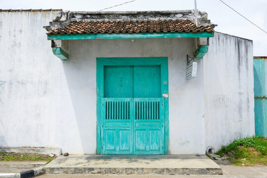 Vintage Chinese Peranakan style entrance gate with green wooden doors, weathered white wall, and tiled roof in Lasem heritage old town, Central Java, Indonesia, reflecting rich cultural history.
