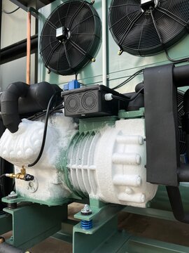 Industrial refrigeration compressor and cooling equipment installed in a factory facility, featuring mechanical components, ventilation fans, piping, and industrial cooling system infrastructure.