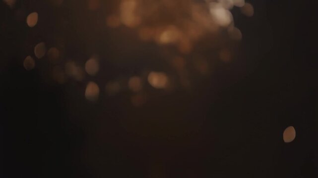 Intentionally blurred warm bokeh particles drift through a dark abstract background. Title sequence, luxury advertising, and event promotion.