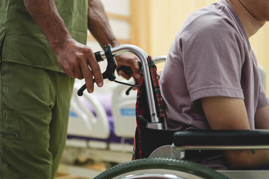 Close-up of caregiver holding handles of wheelchair pushing patient in hospital room, medical care support.