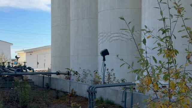 A pan right across an abandoned petroleum bulk plant, showcasing rusted tanks and weathered structures in a semi-rural setting.