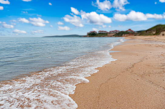A beautiful sandy beach meets gentle ocean waves under a bright blue sky filled with white clouds.