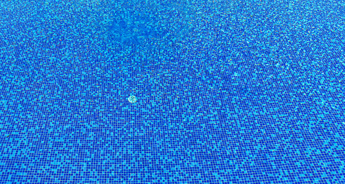 Clear blue water ripples over small mosaic tiles in a outdoor swimming pool.