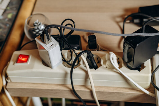 Cluttered Power Strip With Multiple Chargers, Adapters and Cables on Wooden Desk