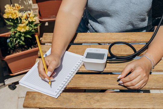 Woman Taking Blood Pressure Reading and Recording Measurements in Notebook on Outdoor Patio