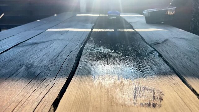 Close-up view of a paintbrush applying dark protective wood stain to a rustic timber table surface. Ideal for DIY guides, wood restoration, and home care tutorials.