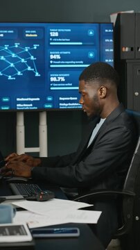 African American young adult software specialist talking on walkie talkie and typing in cybersecurity office. Clip ideal for corporate data protection and network safety campaigns, vertical