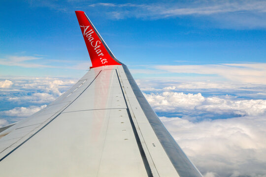An airplane window perspective capturing a commercial winglet and clear blue sky over an expansive cloudscape.