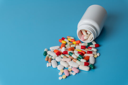 Colorful medical pills and capsules spilling from a white plastic bottle. Healthcare, pharmacy, medication, pharmaceutical industry, treatment concept.