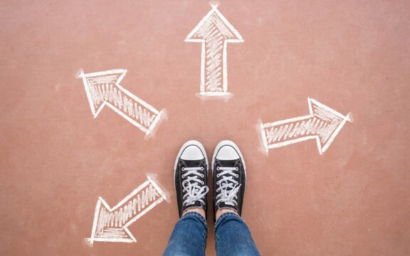 Person wearing black sneakers standing on ground with four white chalk arrows pointing in different directions