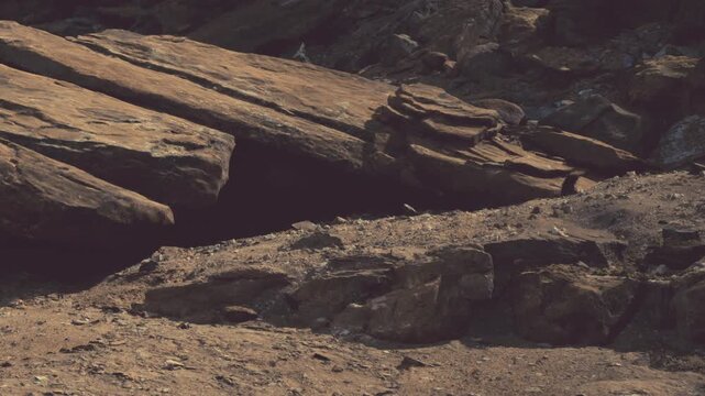 Sunlight bathes a rugged terrain where large, flat rocks jut out from the ground. The dry landscape showcases earthy tones and jagged edges, creating a striking natural scene.