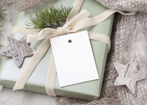 Christmas gift tag mockup on wrapped sage green gift box with fir branch, winter holiday scene
