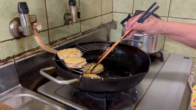 サツマイモの天ぷらを揚げる高齢女性の手