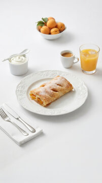 Apricot strudel accompanied by a cup of coffee, orange juice, and fresh fruit for breakfast