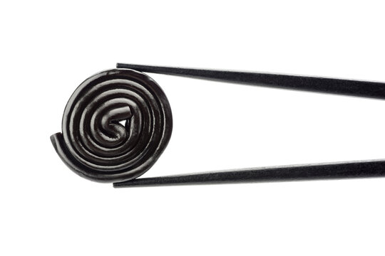 Liquorice wheel single between black chopsticks, isolated on white background.