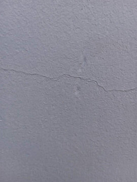 Cracked plaster wall with a single fracture line pale gray texture