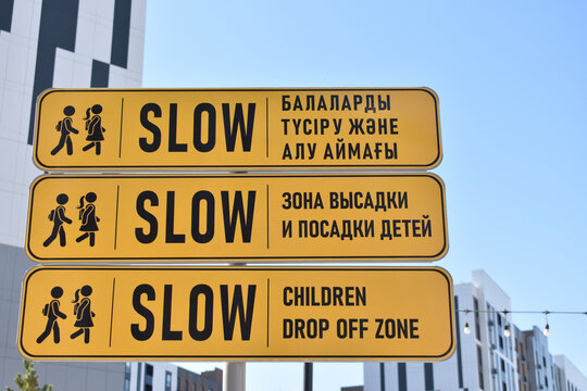 Yellow road signs for children drop off zone with Slow text in three languages (Kazakh, Russian, English). School safety concept