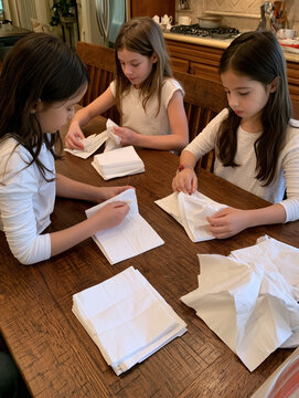 Three girls folding white napkins at kitchen table