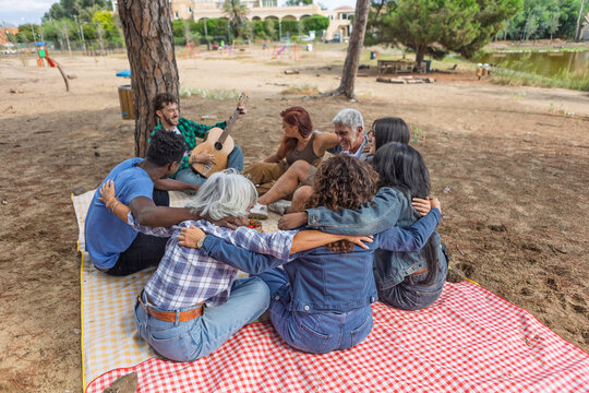 Friends embracing in a circle around a man playing acoustic guitar