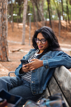 Young woman in glasses texting on a smartphone on a park bench