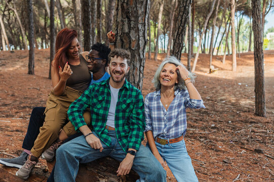 Four friends laughing together while sitting on a log in the woods
