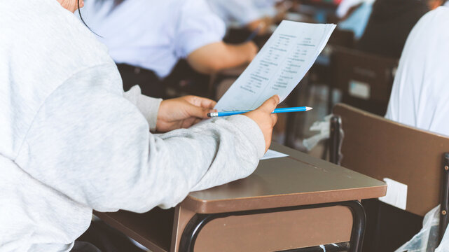 Students writing and reading exam answer sheets exercises in classroom of school with stress