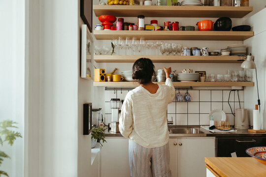 Rear view of woman taking mug from shelf in kitchen while living simple life at home