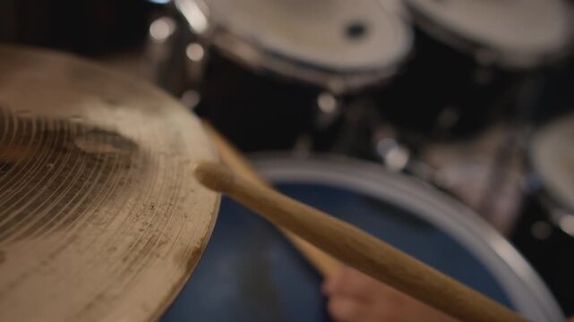 Teenage musician striking drum kit cymbal with wooden drumstick during rehearsal in extreme close up. Footage suits music school advertising, youth band promos, and tutorial videos