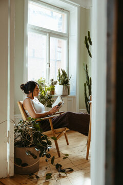 Woman reading book while sitting on chair and spending leisure time in home