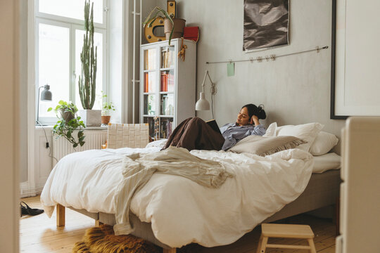 Carefree woman spending leisure time reading book while lying on bed in home