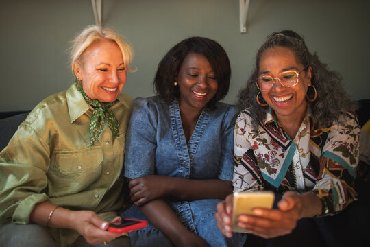 Happy female friends enjoying leisure time on smart phone at home