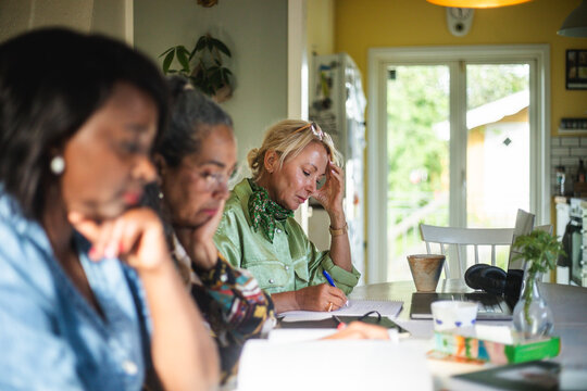 Senior woman writing in book while studying with friends at home