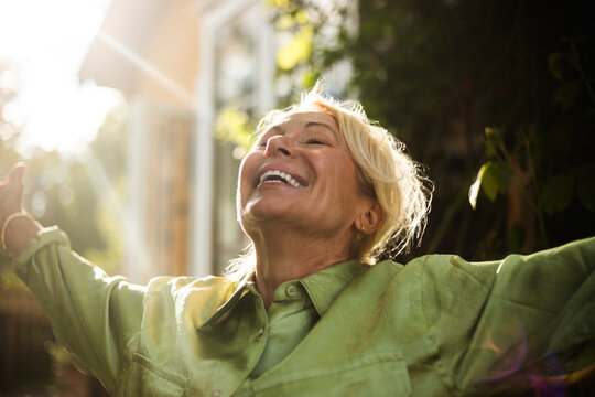 Carefree senior woman enjoying fresh air with arms outstretched in back yard
