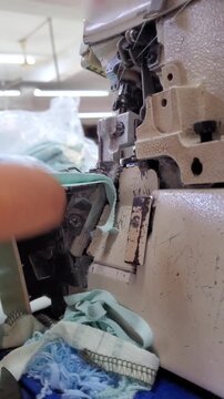 Close up of industrial overlock sewing machine stitching fabric in garment factory
