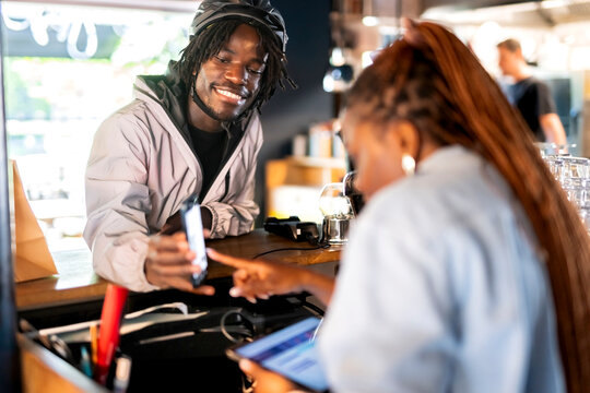 Smiling delivery man showing order details on smart phone to restaurant owner