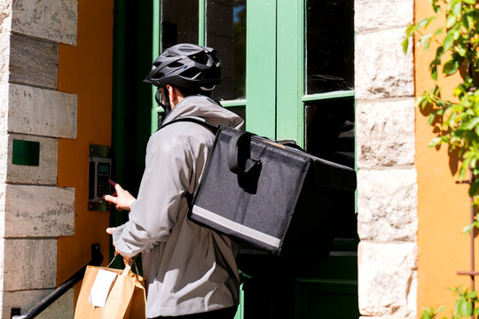 Male delivery worker carrying thermal bag ringing intercom at building entrance