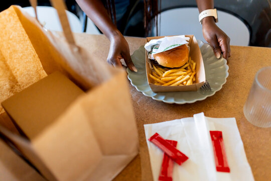High angle view of woman keeping plate of burger and french fries on table at home